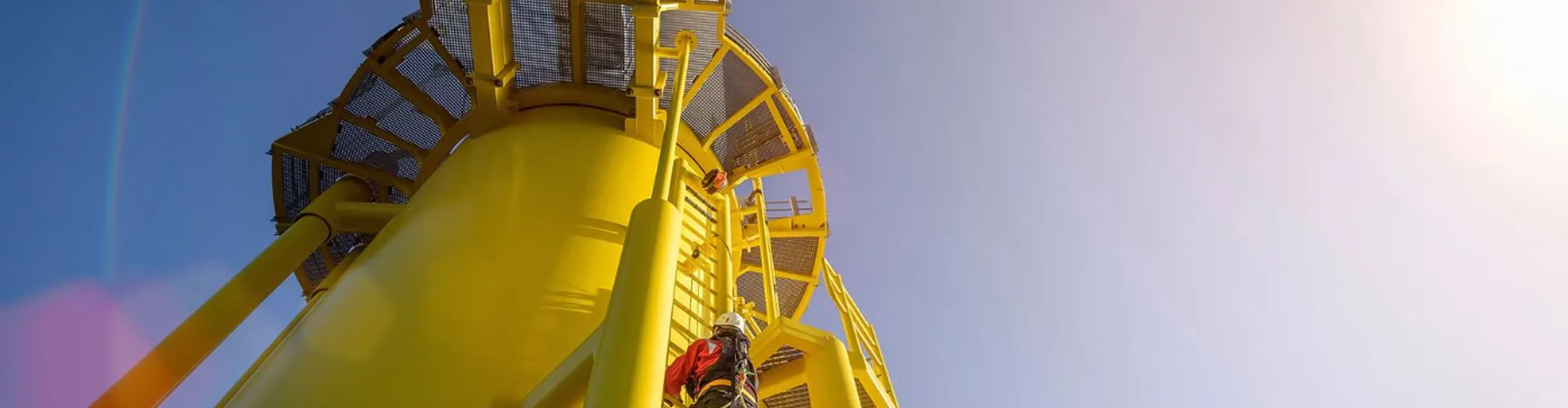Worker climbing a yellow wind turbine tower.